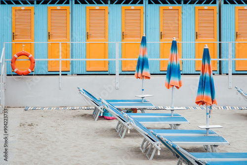 Fototapeta Naklejka Na Ścianę i Meble -  cabines de plage et chaises longues sur une plage italienne. Cabines de plage bleues et oranges alignées. Bains de soleil et parasols de couleur en Italie. Vacances à la mer