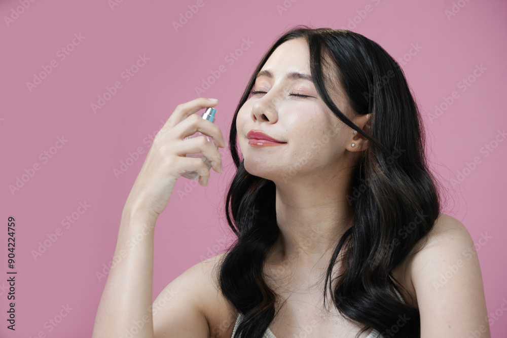 Obraz premium Beautiful Asian woman with Korean style makeup holding a bottle of perfume smelling the fragrance on a pink background