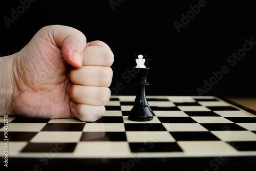 A fist against a black king on a chessboard on a black background close-up, brute force versus mind, overthrowing the ruler, government ultimatum,