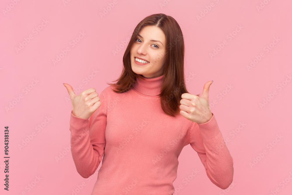 Cheerful happy attractive woman with brown hair keeping thumb raised, being in good mood, showing her agreement, wearing rose turtleneck. Indoor studio shot isolated on pink background Cheerful happy attractive woman with brown hair keeping thumb raised, being in good mood, showing her agreement, wearing rose turtleneck. Indoor studio shot isolated on pink background