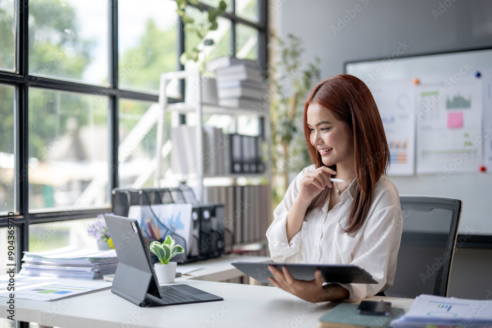 A woman is sitting at a desk with a tablet in her hand A woman is sitting at a desk with a tablet in her hand
