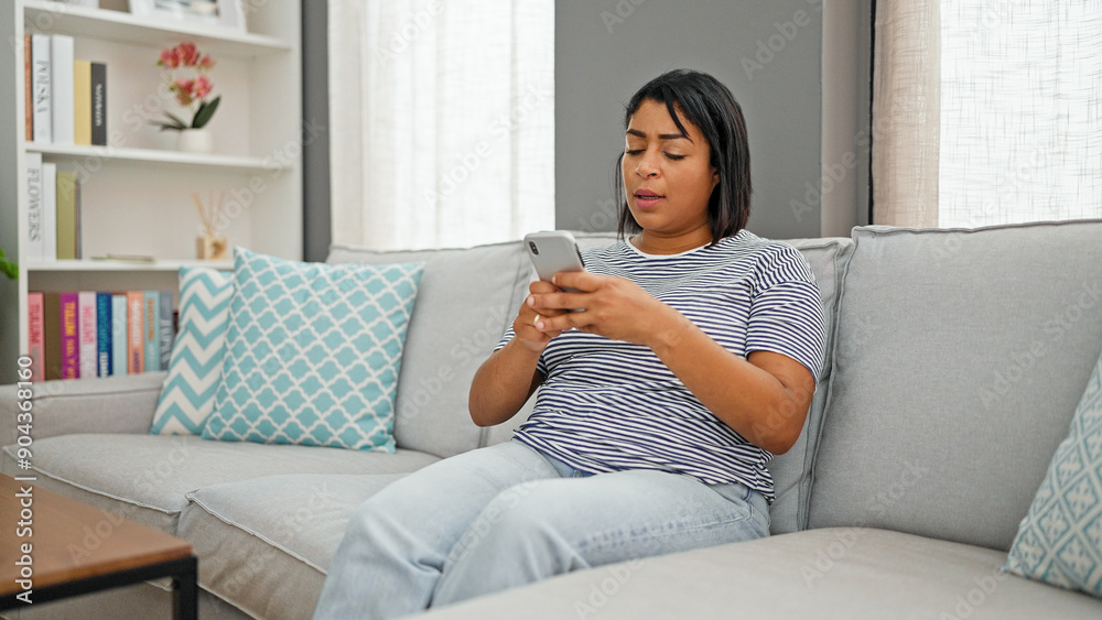 Hispanic woman relaxing on couch with smartphone in a modern living room Hispanic woman relaxing on couch with smartphone in a modern living room