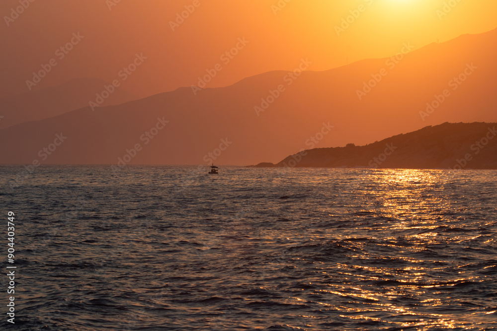 Small fisherboat on the wild island of Ikaria with mountain slopes and orange sky at sunrise, North Aegean Sea, Greece Small fisherboat on the wild island of Ikaria with mountain slopes and orange sky at sunrise, North Aegean Sea, Greece
