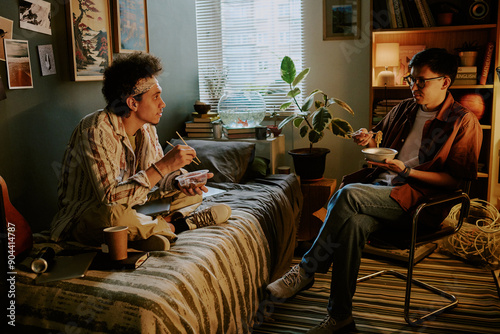 Φωτογραφία Biracial roomies eating Chinese instant noodles and chatting in their dorm room