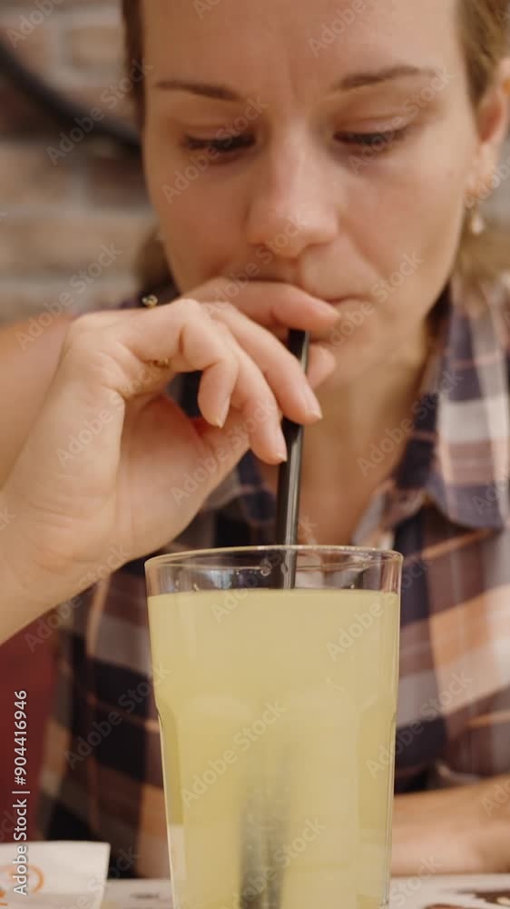 Vertical video. Woman Enjoys a Refreshing Drink with a Straw in a Cozy Cafe, Brick Walls Adding to the Charming Atmosphere. Vertical video. Woman Enjoys a Refreshing Drink with a Straw in a Cozy Cafe, Brick Walls Adding to the Charming Atmosphere.