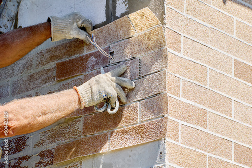 Installing brick veneer outside, construction worker decorates facade of house with exterior panel of fake thin brick.