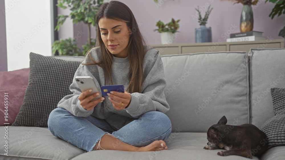 Young hispanic woman with credit card and phone shopping online beside her pet chihuahua at home. Young hispanic woman with credit card and phone shopping online beside her pet chihuahua at home.