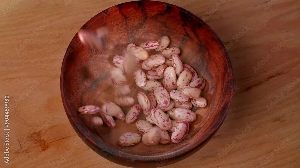 Unprocessed pinto beans falling into a wooden bowl, in slow motion.