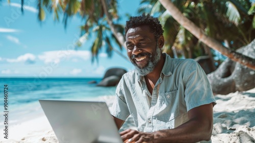 A mature man is joyfully laughing as he works on his laptop on a stunning white sandy beach, pairing the beauty of a beachside setting with a productive remote work environment. © ChaoticMind