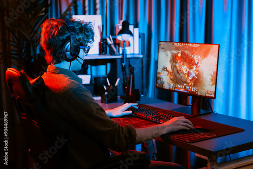 Host channel of young gaming streamer playing fighting Moba at battle arena game with multiplays team, wearing headphone on pc monitor with back side image at neon digital light modern room. Gusher.