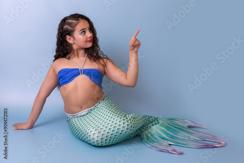 Tableau sur toile A child girl in a mermaid costume sits on a blue background