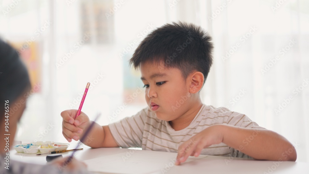 A boy is writing with a pink pencil on a piece of paper A boy is writing with a pink pencil on a piece of paper