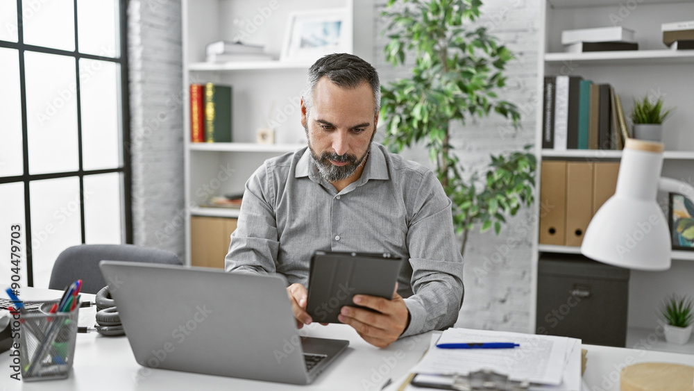 Handsome senior hispanic man with beard and grey hair using tablet in modern office Handsome senior hispanic man with beard and grey hair using tablet in modern office