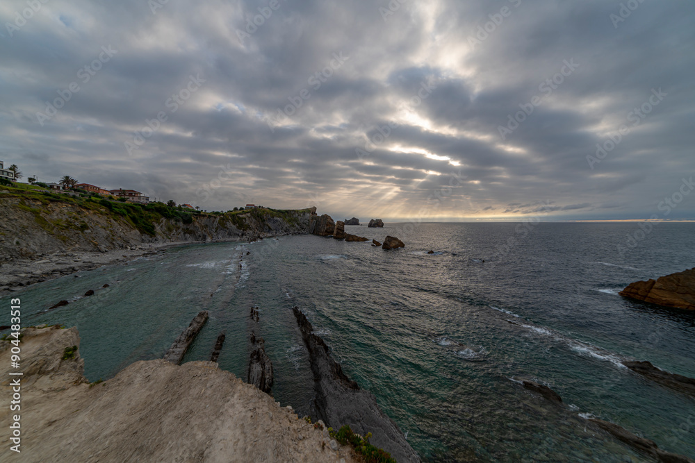 Beautiful sunset over Playa de la Arnía, featuring dramatic skies, rocky shoreline, and coastal homes in Cantabria, Spain. Perfect for seascape, travel, and nature themes. Beautiful sunset over Playa de la Arnía, featuring dramatic skies, rocky shoreline, and coastal homes in Cantabria, Spain. Perfect for seascape, travel, and nature themes.