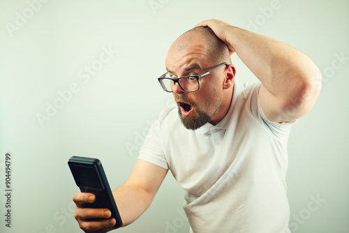 Portrait of surprised handsome bearded man with glasses and white shirt looking at mobile phone, facial expression, isolated on white background