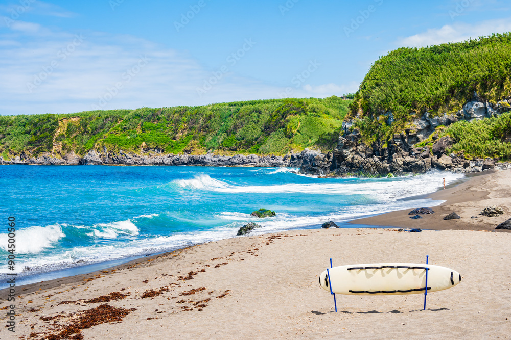 Surfing board on idyllic beach and waves on ocean coast in Moinhos village, Sao Miguel island, Azores, Portugal Surfing board on idyllic beach and waves on ocean coast in Moinhos village, Sao Miguel island, Azores, Portugal