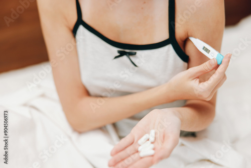 Woman holding thermometer on bed with pillows and white sheet covering body photo