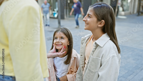 A candid moment as two smiling young girls engage with a woman on a bustling city street.