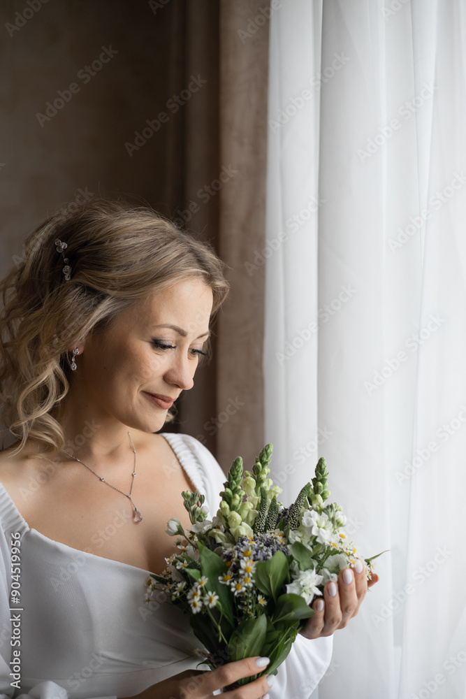 Bride with beautiful hairstyle and make-up wearing white wedding dress stands at the window with her bouquet. She is awaiting the arrival of the groom. Preparing for the wedding ceremony Bride with beautiful hairstyle and make-up wearing white wedding dress stands at the window with her bouquet. She is awaiting the arrival of the groom. Preparing for the wedding ceremony