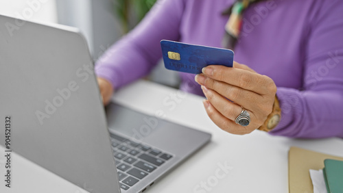 Mature woman holding credit card in office setting, ready for online transaction.