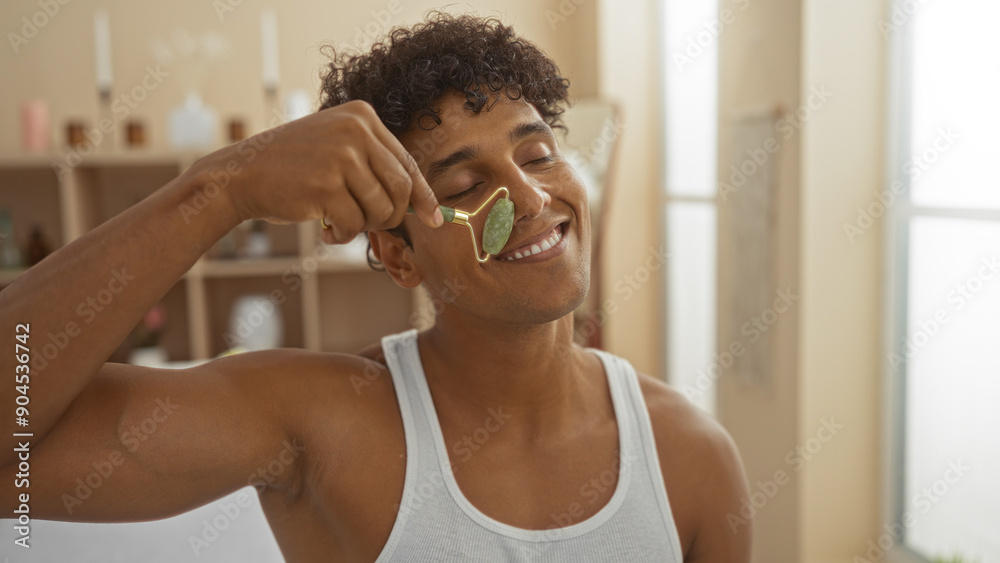 Handsome young man using jade roller in wellness spa room for facial massage