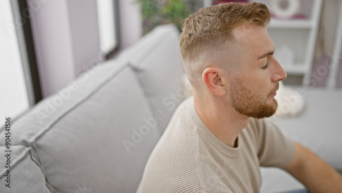 Caucasian man with beard sitting thoughtfully in a modern living room interior, embodying relaxation and casual lifestyle.