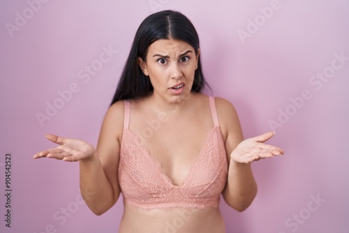 Young hispanic woman wearing pink bra clueless and confused with open arms, no idea concept. photo