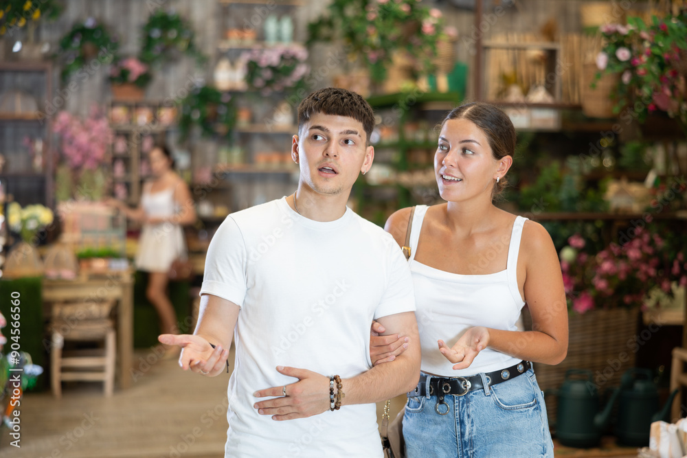 Naklejka premium Positive friendly young adult couple, guy and girl, looking with interest for comfortable furniture for patio and garden of country house in home decor store