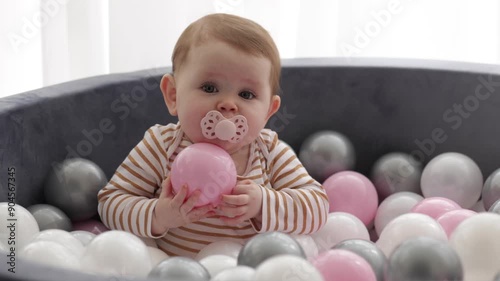 Toddler having fun playing in ball pit with pink, white, and gray balls