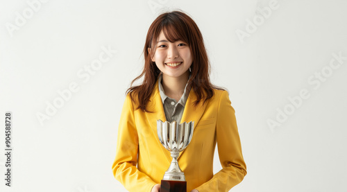 A young Smiling Asain woman dressed in a gold business suit smiles brightly as she holds a golden trophy. Her confident pose and happy expression convey a sense of accomplishment photo