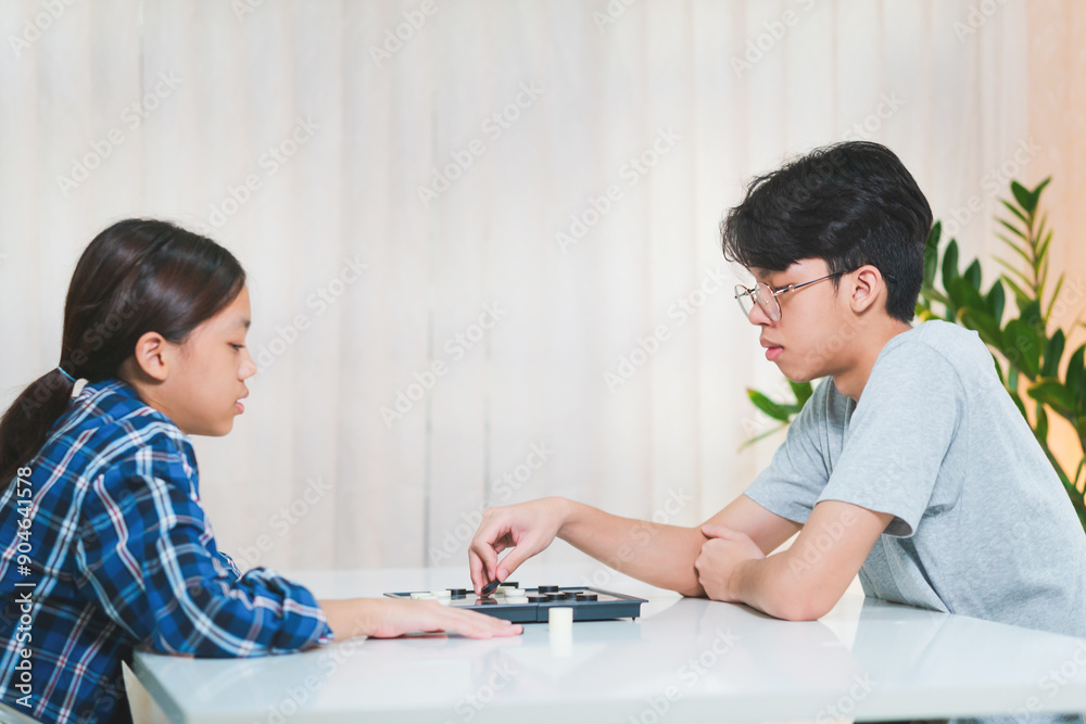 Asian teenage boy and girl playing board game, Asian brother and sister relaxing hobbies playing a game of checkers Asian teenage boy and girl playing board game, Asian brother and sister relaxing hobbies playing a game of checkers