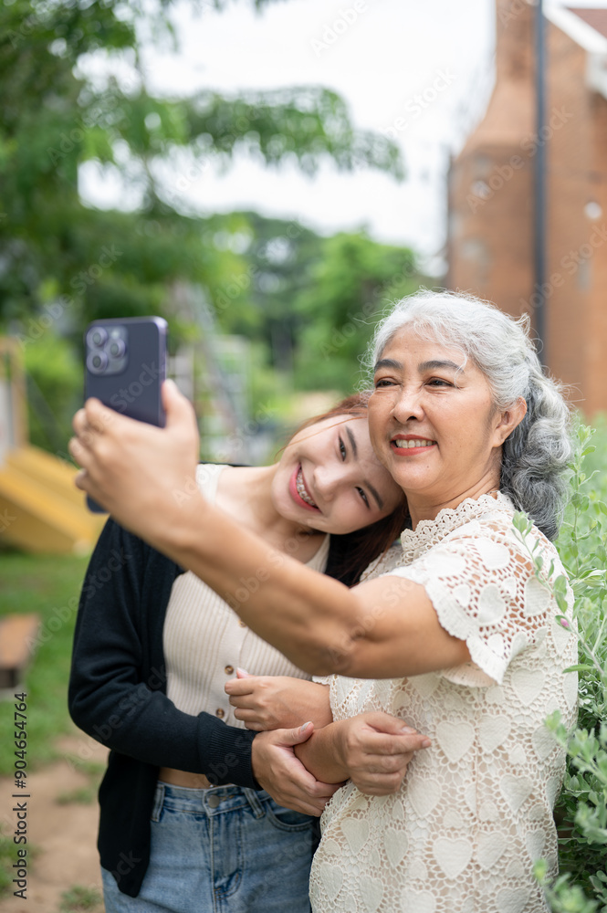A lovely Asian grandma is taking a selfie with her granddaughter while chilling together in a garden A lovely Asian grandma is taking a selfie with her granddaughter while chilling together in a garden