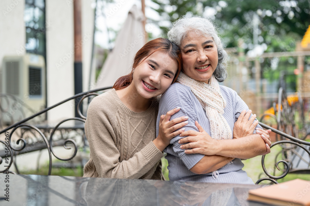 Naklejka premium A lovely Asian granddaughter and a happy grandma are sitting at a table outdoors together.
