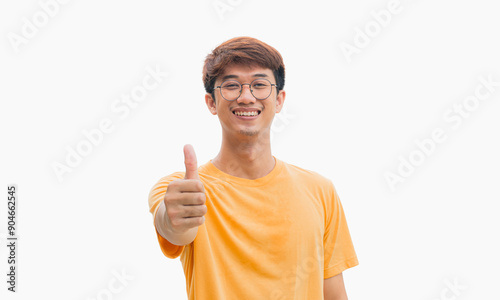 A young Asian man in his 20s wearing a yellow t-shirt with a smile pointing thumbs up isolated on a gray background. Well done. Agreement concept. Happy man