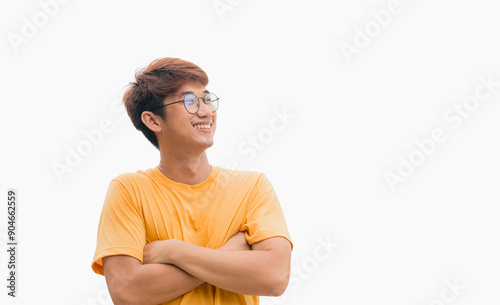 A young Asian man in his 20s wearing a yellow t-shirt stands confidently with his arms crossed over his chest, isolated on a gray background. Positive person.