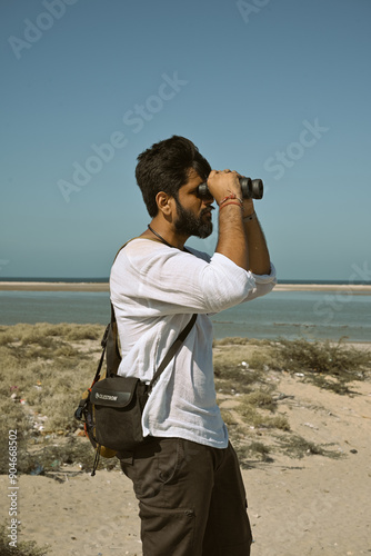 man looking through binoculars on the beach