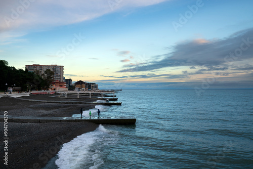 View of the Black Sea coast and the pebble beach with breakwaters along the Prosveshcheniya Street in Adler at sunset on a sunny day, Adler, Sochi, Krasnodar Territory, Russia photo