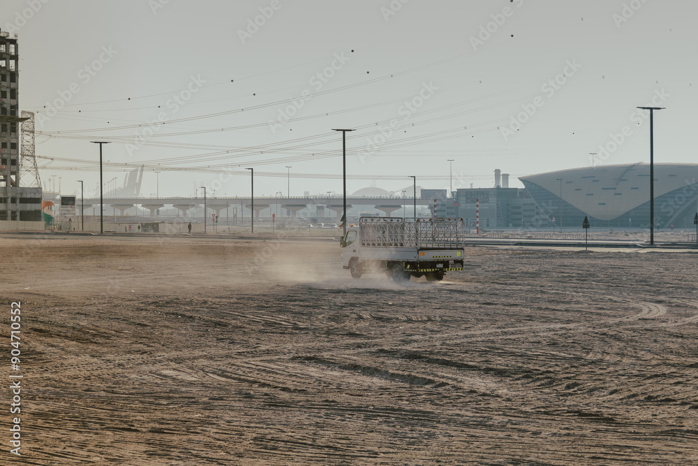 Truck driving through desert terrain with city infrastructure in the background Truck driving through desert terrain with city infrastructure in the background