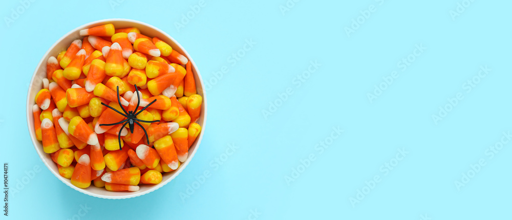 Fototapeta premium Bowl with tasty Halloween candy corns and spider on light blue background with space for text
