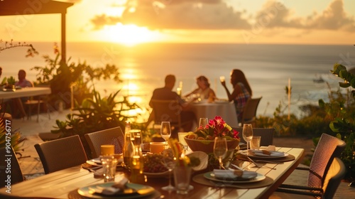 Group of people enjoying a meal at an outdoor dining table with a stunning ocean view, bathed in the warm glow of a sunset.