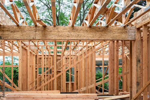 New house construction in residential neighborhood, job site detail, first floor interior wood framing installed, looking up at wood truss support beams for second floor, summer day on job site
