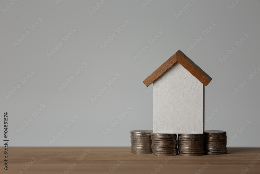 Planning and saving money for purchasing a home and choosing to invest in real estate. wooden house model Stacked coins on a wooden table Planning and saving money for purchasing a home and choosing to invest in real estate. wooden house model Stacked coins on a wooden table