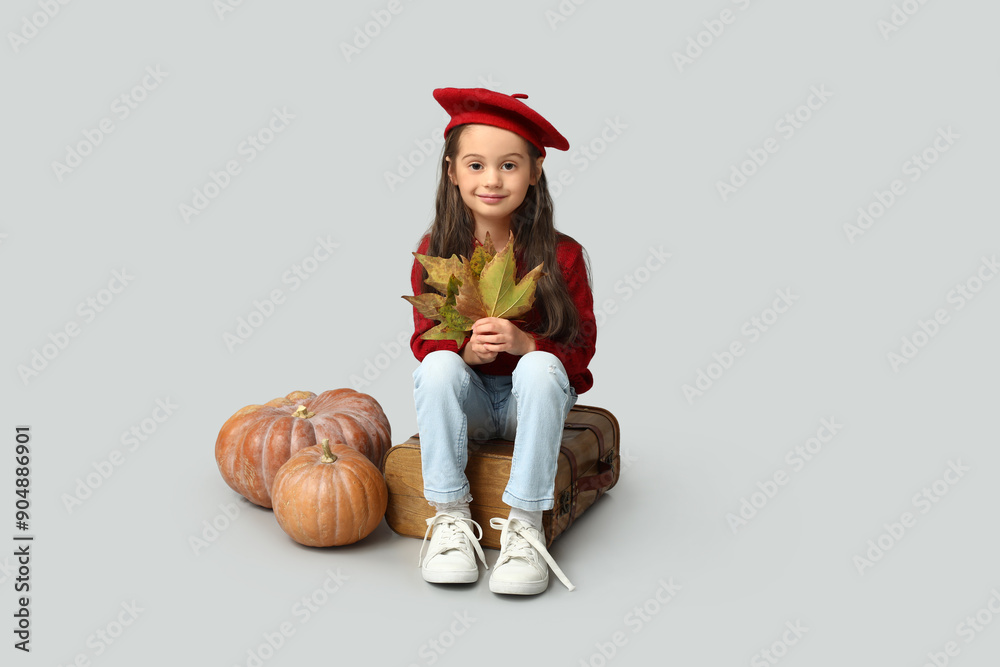 Cute little girl in stylish clothes with autumn leaves, pumpkins and suitcase on grey background Cute little girl in stylish clothes with autumn leaves, pumpkins and suitcase on grey background