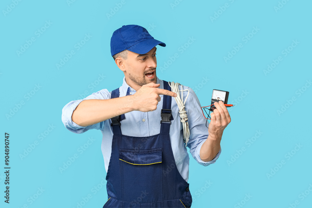 Portrait of male electrician with wires pointing at multimeter on blue background Portrait of male electrician with wires pointing at multimeter on blue background