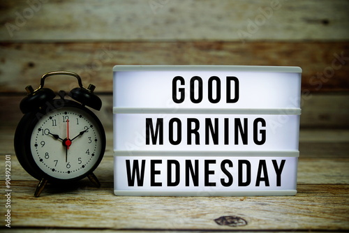 Good Morning Wednesday text on LED lightbox with alarm clock on wooden background