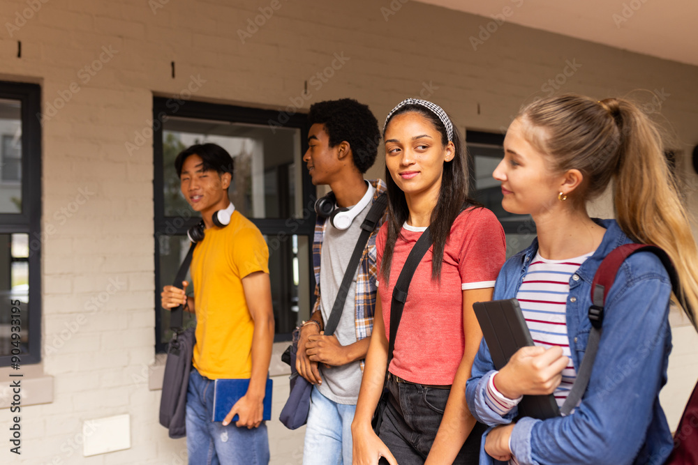 Standing outside high school building, teenagers carrying backpacks and books Standing outside high school building, teenagers carrying backpacks and books