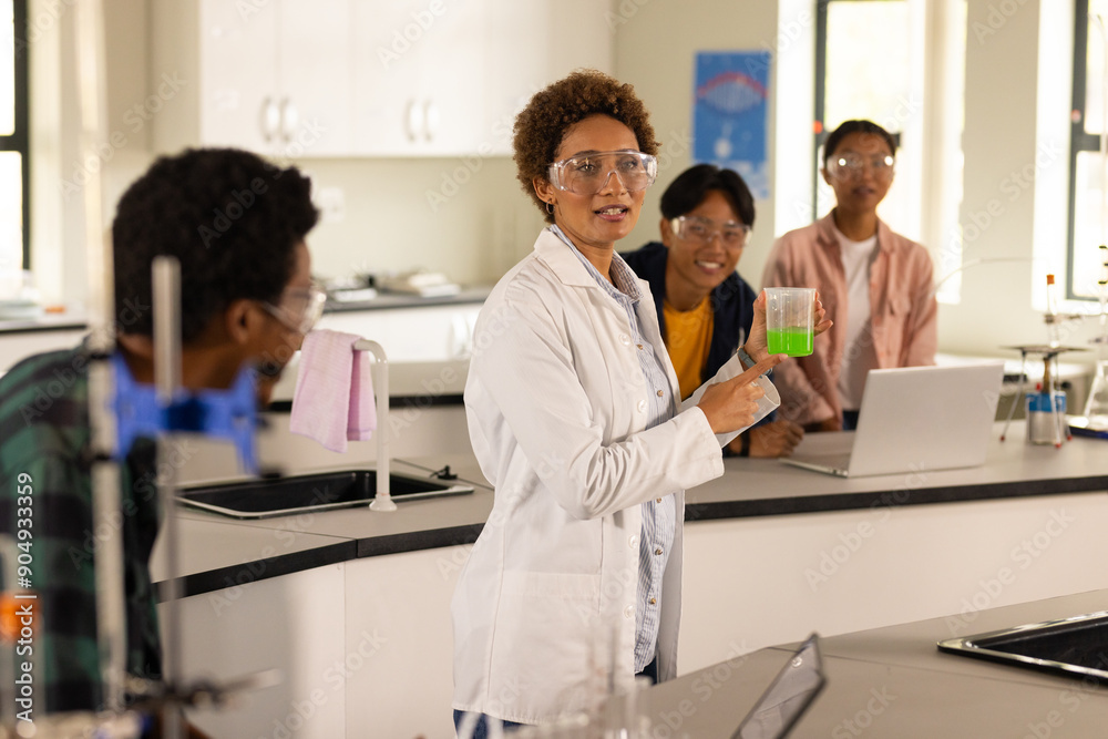 In high school laboratory, teacher demonstrating experiment with beaker to students In high school laboratory, teacher demonstrating experiment with beaker to students