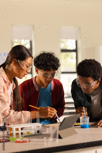 Conducting science experiment, teenagers using tablet and lab equipment in high school