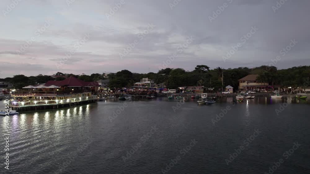 Aerial view of a beachfront with a lit-up dock and countless people enjoying their evening in Roatan, Honduras. Aerial view of a beachfront with a lit-up dock and countless people enjoying their evening in Roatan, Honduras.