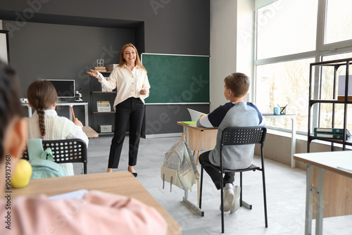 Mature teacher conducting lesson to little pupils in classroom